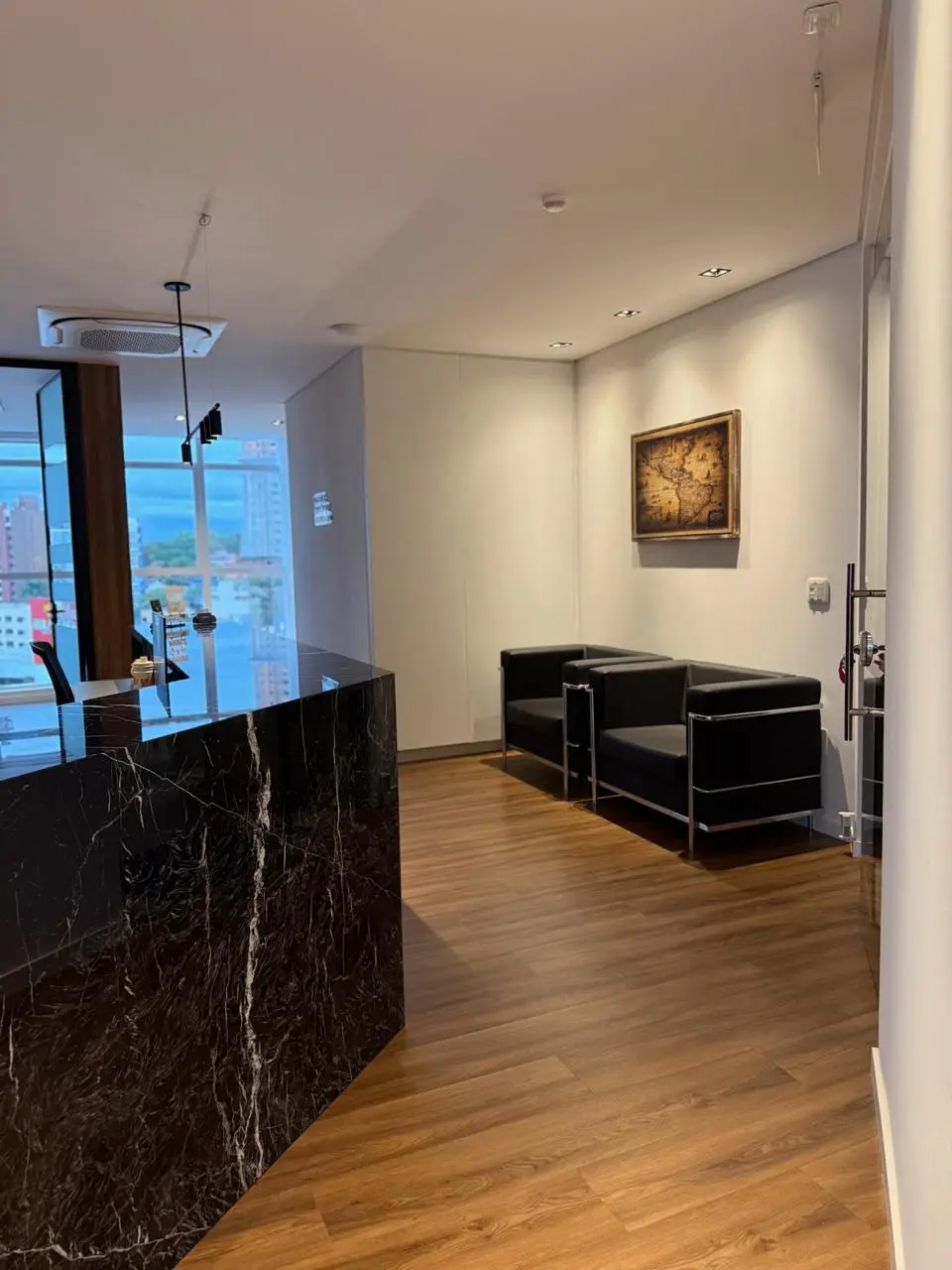 Sala de espera com poltronas de couro preto, quadro com mapa antigo e o balcão de mármore preto da recepção.